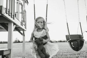 Black and white image of child playing near swing set with wind blowing through hair.