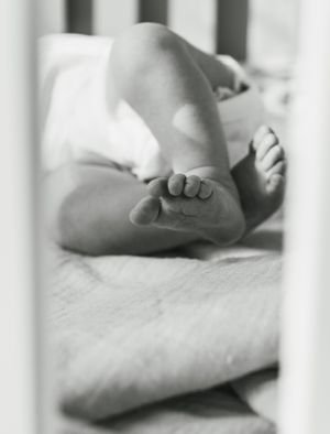 Close-up black and white photo of tiny baby feet through crib slats.