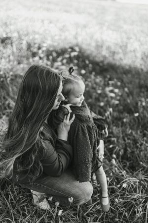 A black and white portrait of a mother and child sitting together in a wildflower meadow.