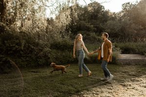 Couple walking their dog on a sunlit nature trail during golden hour.