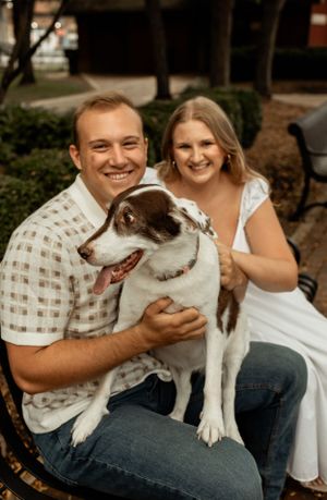 A couple poses with their happy black and white dog on a park bench.