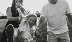 Joyful outdoor family moment captured in black and white as child leaps between parents.