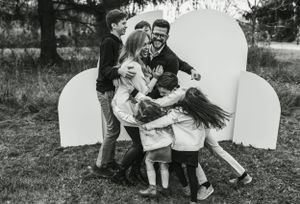 Black and white candid family moment with children laughing against white backdrop outdoors.
