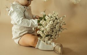 A small child in white clothing sits with white baby's breath flowers.