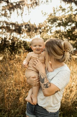 A tender sunset moment captured between parent and baby in golden sunlit field with tall grass.
