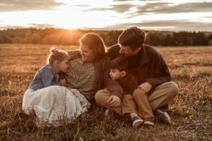 A family sits together in a grassy field during golden hour sunset.
