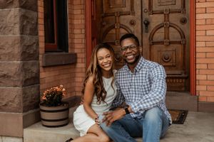 A couple sitting and smiling together on stone steps in front of an ornate wooden door.