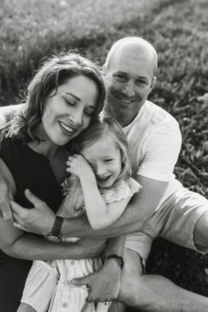 Candid black and white family portrait showing shared laughter and embraces on grassy field.