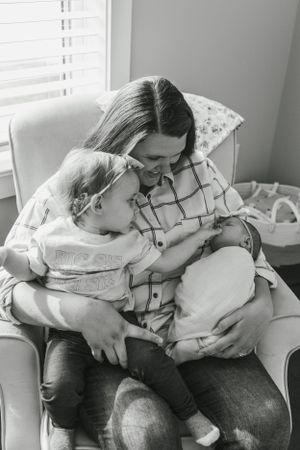 Intimate black and white photo showing tender family moment in a cozy armchair with newborn.