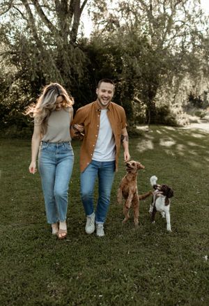Casual couple walking dogs on grassy lawn in backyard garden setting.