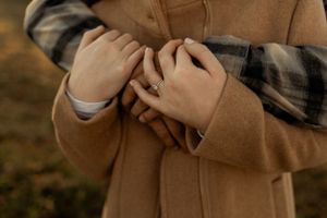 Close-up shot of hands holding each other with a beige coat and plaid shirt in view.