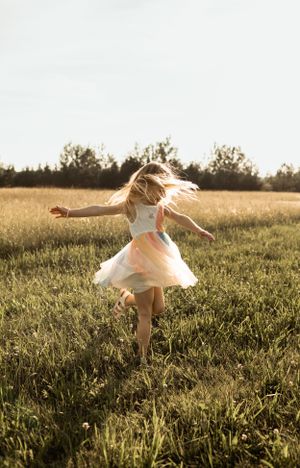 Young dancer twirling in white dress during golden hour in grassy field.