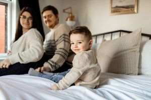 A relaxed family scene in a bright, modern bedroom with neutral decor.