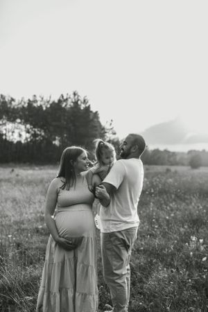 A family shares an intimate outdoor moment in a field during a maternity photoshoot.