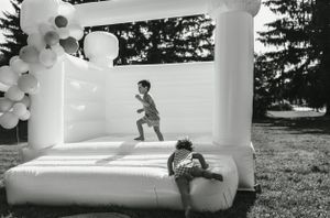 Children having fun jumping and playing in a white bounce house decorated with balloons.