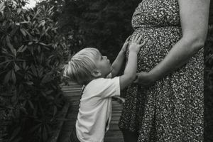 Black and white image showing tender moment between child and expectant parent.
