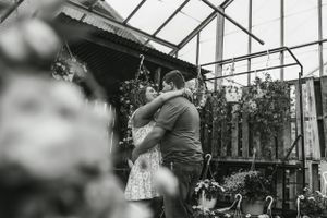 A romantic black and white embrace in front of a greenhouse structure.