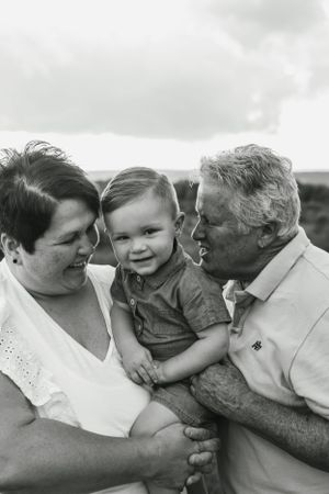 Black and white family portrait showing three generations sharing affectionate moment outdoors.
