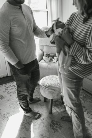 A couple stands in their home looking down at something together while a cat sits nearby.