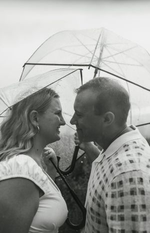 A couple shares an intimate moment under a clear umbrella in black and white photography.