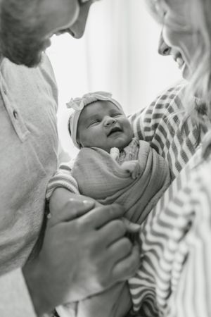 A newborn baby smiles while being held in black and white portrait.