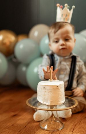 First birthday celebration with smiling baby wearing crown next to small white cake.