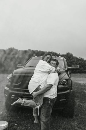 A loving couple embraces in front of a black truck in a casual outdoor setting.