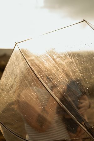 Close-up of raindrops on clear umbrella with golden sunlight shining through.
