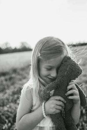 Sweet black and white portrait of child hugging teddy bear in outdoor setting.