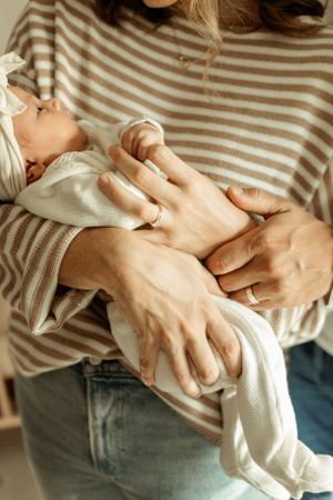 Close-up of hands gently cradling a newborn baby wrapped in white fabric.