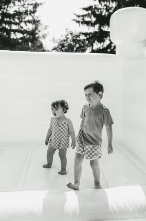 Two children play together on a white bouncy castle surface on a sunny day.