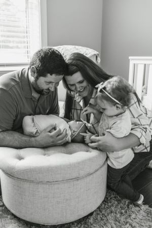 Black and white photo of family sharing an intimate moment together on a round ottoman.