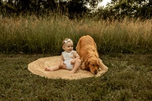 A golden retriever rests beside a small figure on a circular rug outdoors in natural lighting.