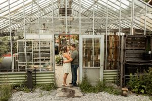 A romantic moment captured outside a rustic greenhouse with soft natural lighting.
