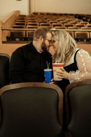 A couple shares an intimate moment in an empty auditorium with drinks.
