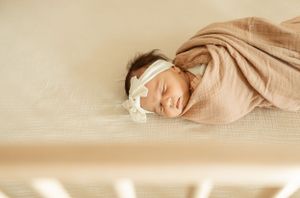 A sleeping newborn wrapped in beige fabric rests peacefully on a light background.