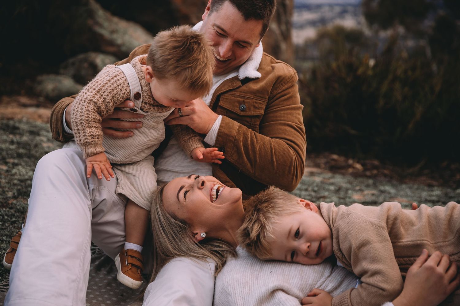 Joyful family of four laughing and playing together outdoors with two young toddlers.