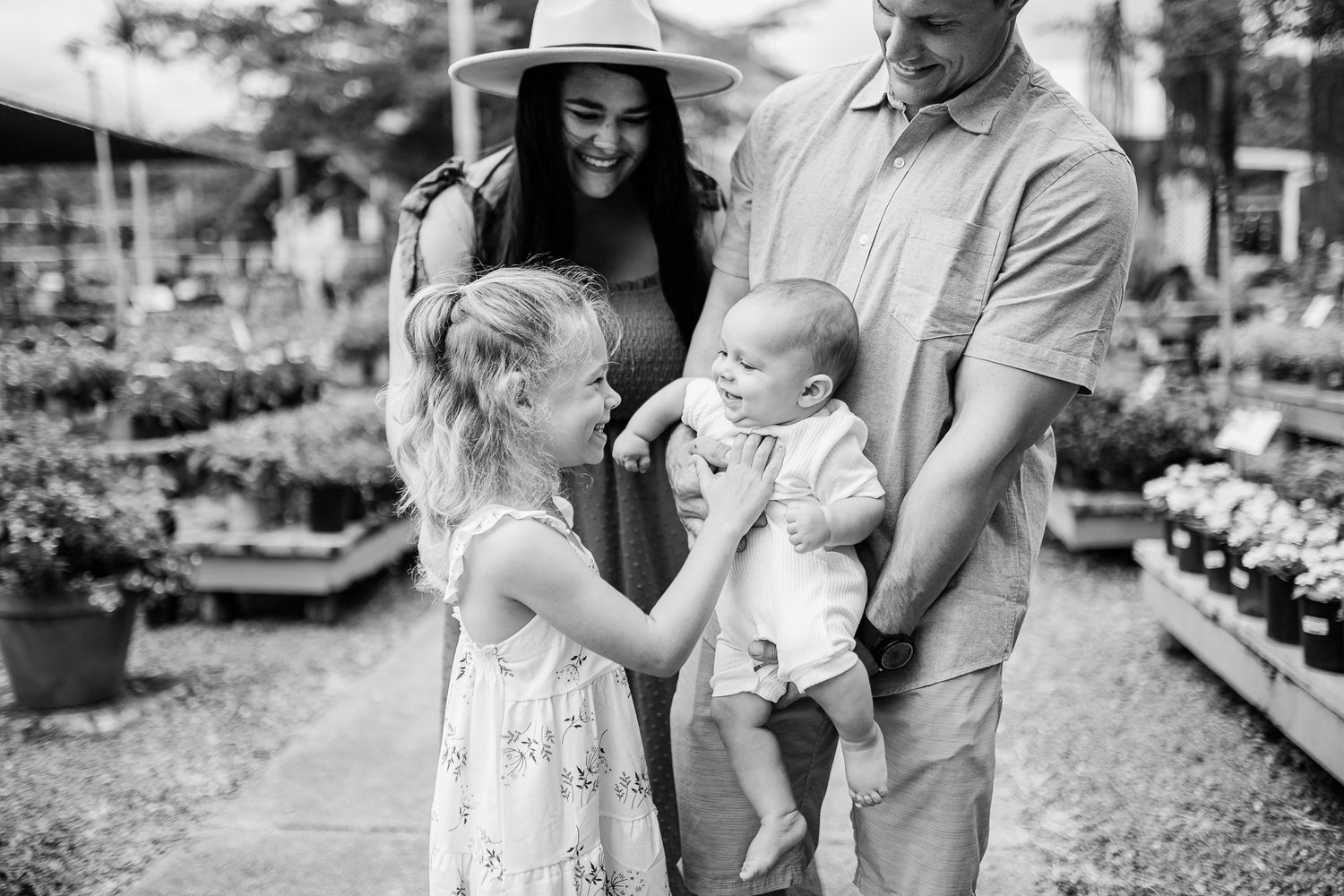 Black and white family portrait at garden nursery with young children.