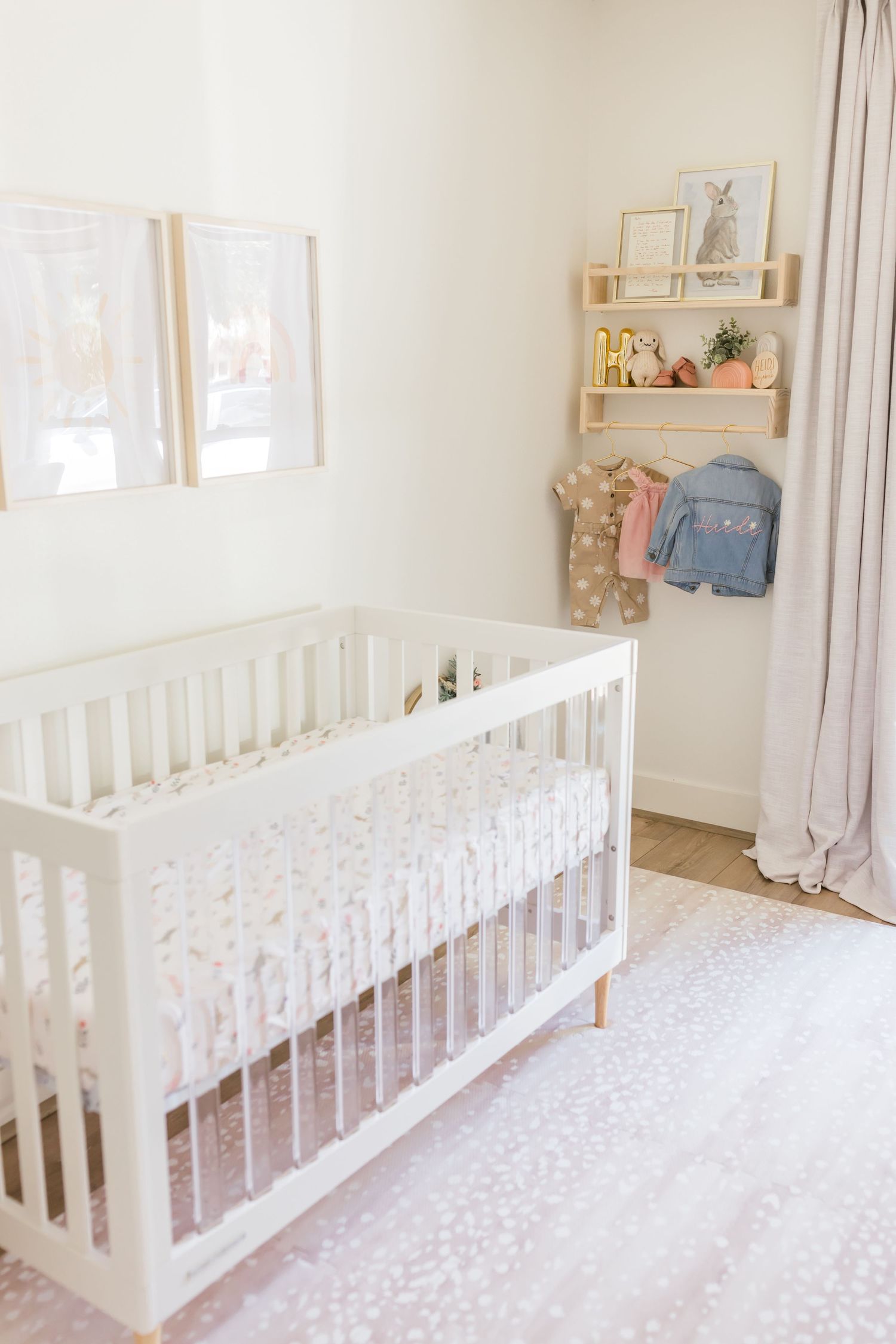 Modern white nursery with crib, pink rug and wall art in minimalist style.