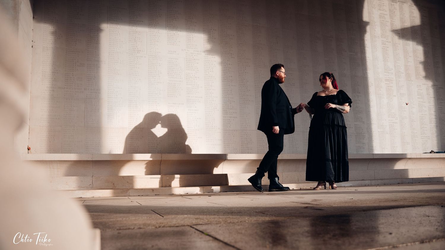Couple casting heart-shaped shadow on wall while holding hands at monument.