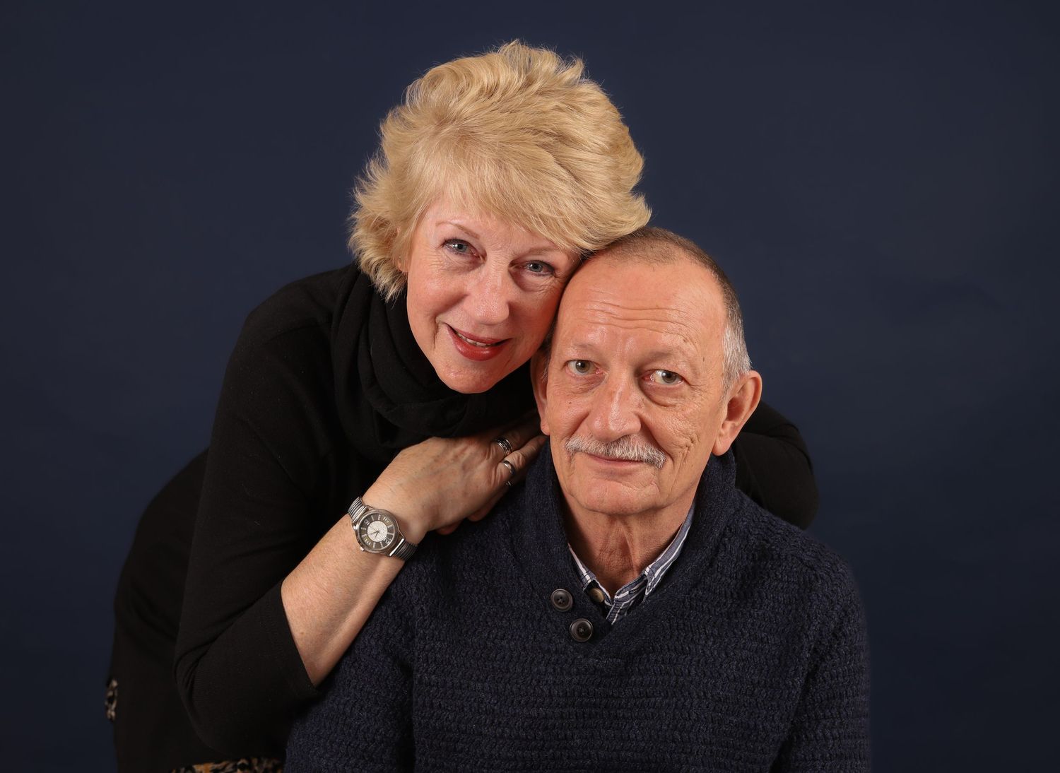 Senior couple smiles together against dark background in studio portrait.