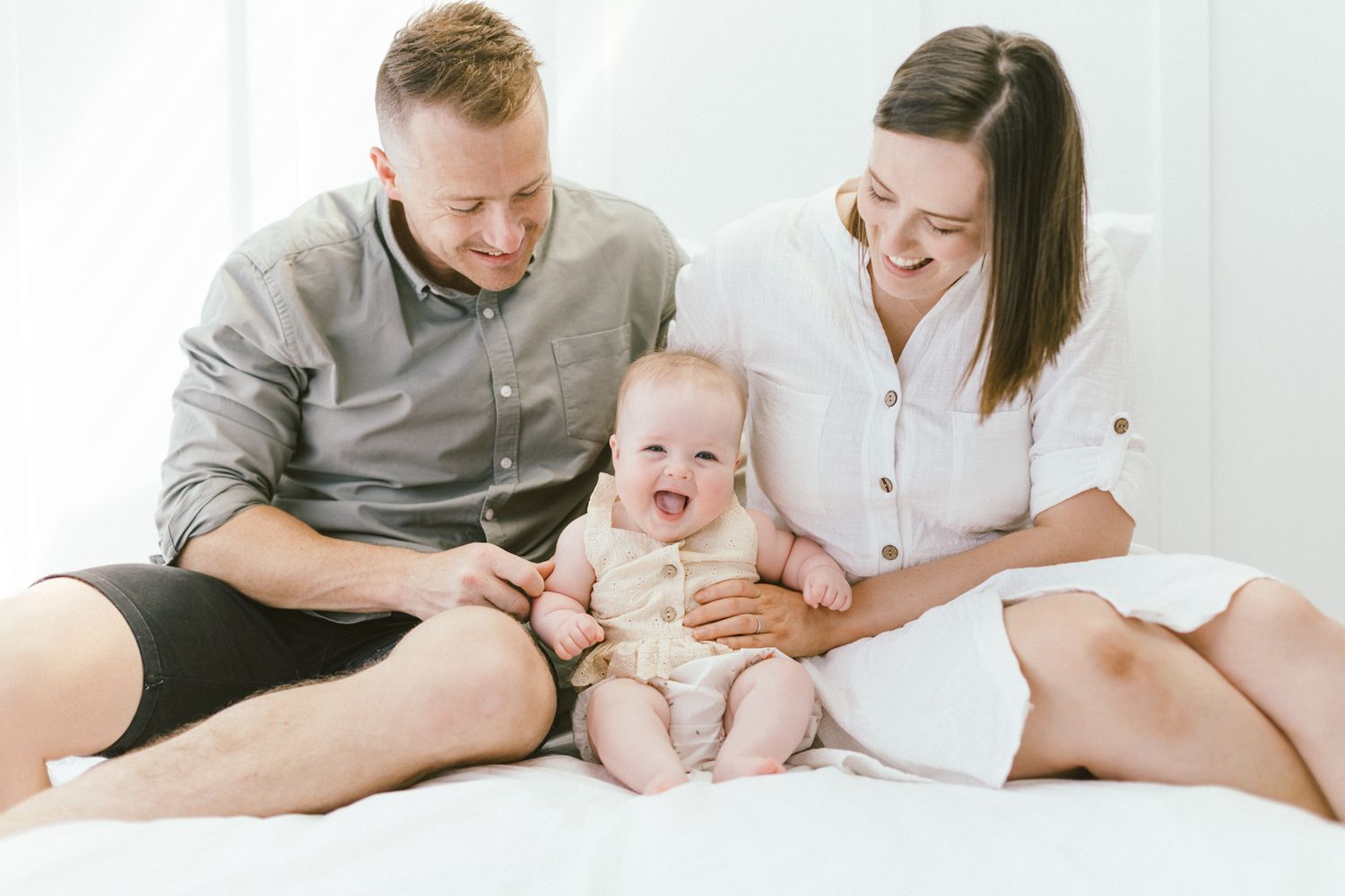 Family cuddles together on floor during bright white lifestyle photography session.