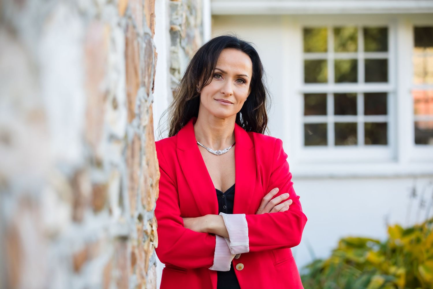 Outdoor portrait against stone wall featuring bright red blazer and casual business attire.
