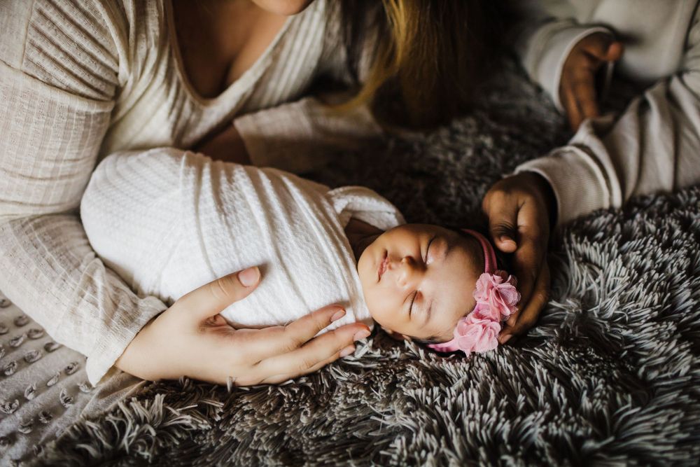 Tender portrait of sleeping baby in white clothing on soft gray blanket.