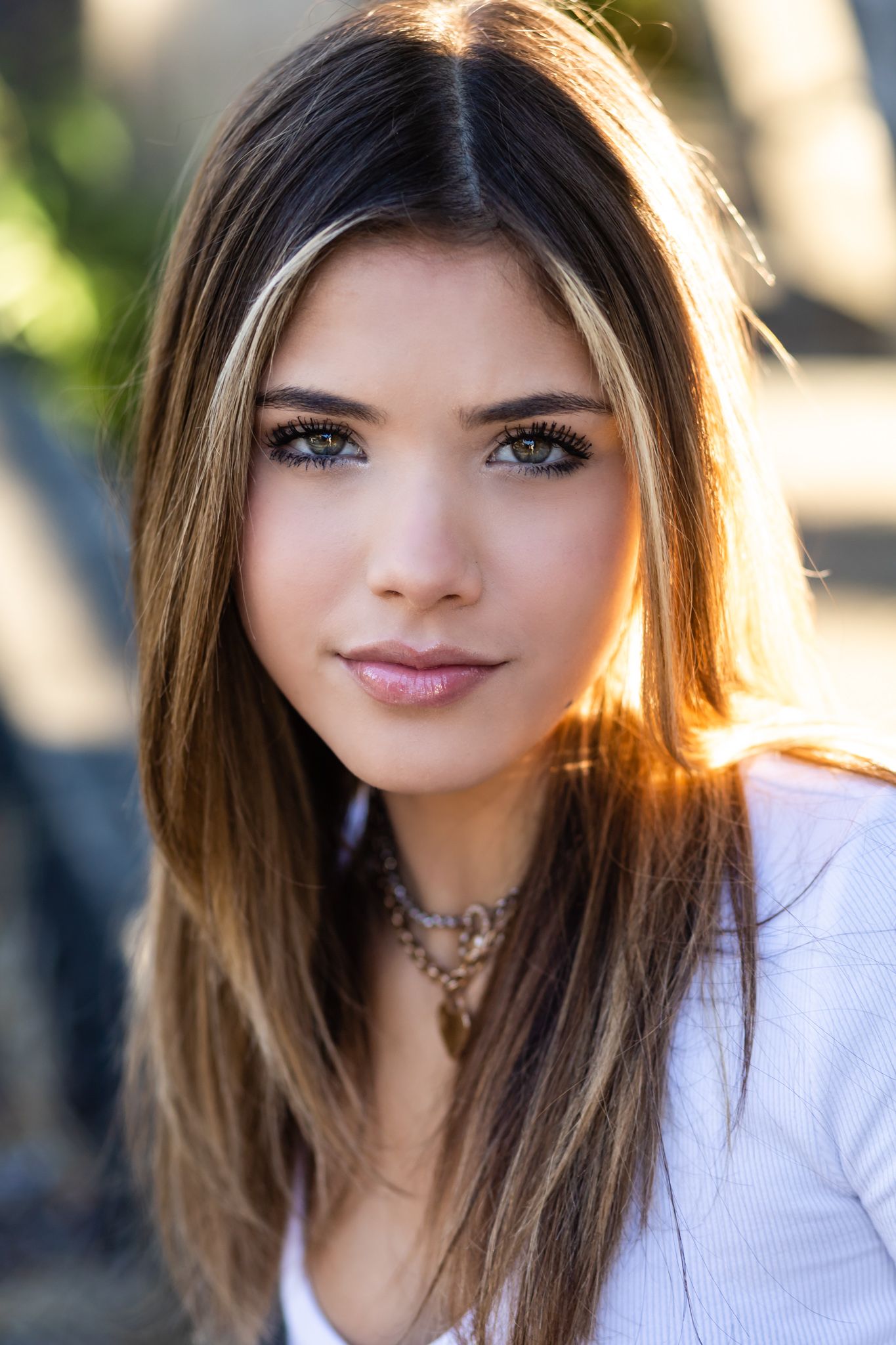 Portrait of person in white top and delicate necklace with sunlit background.