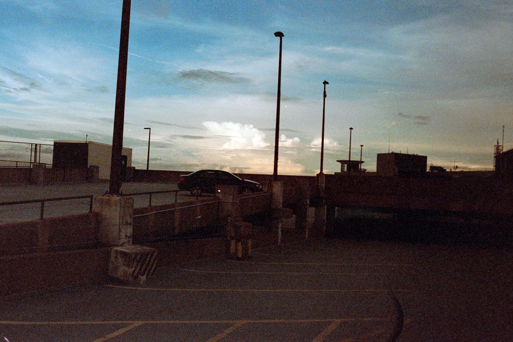 Empty parking lot at dusk with light poles casting shadows against the darkening sky.
