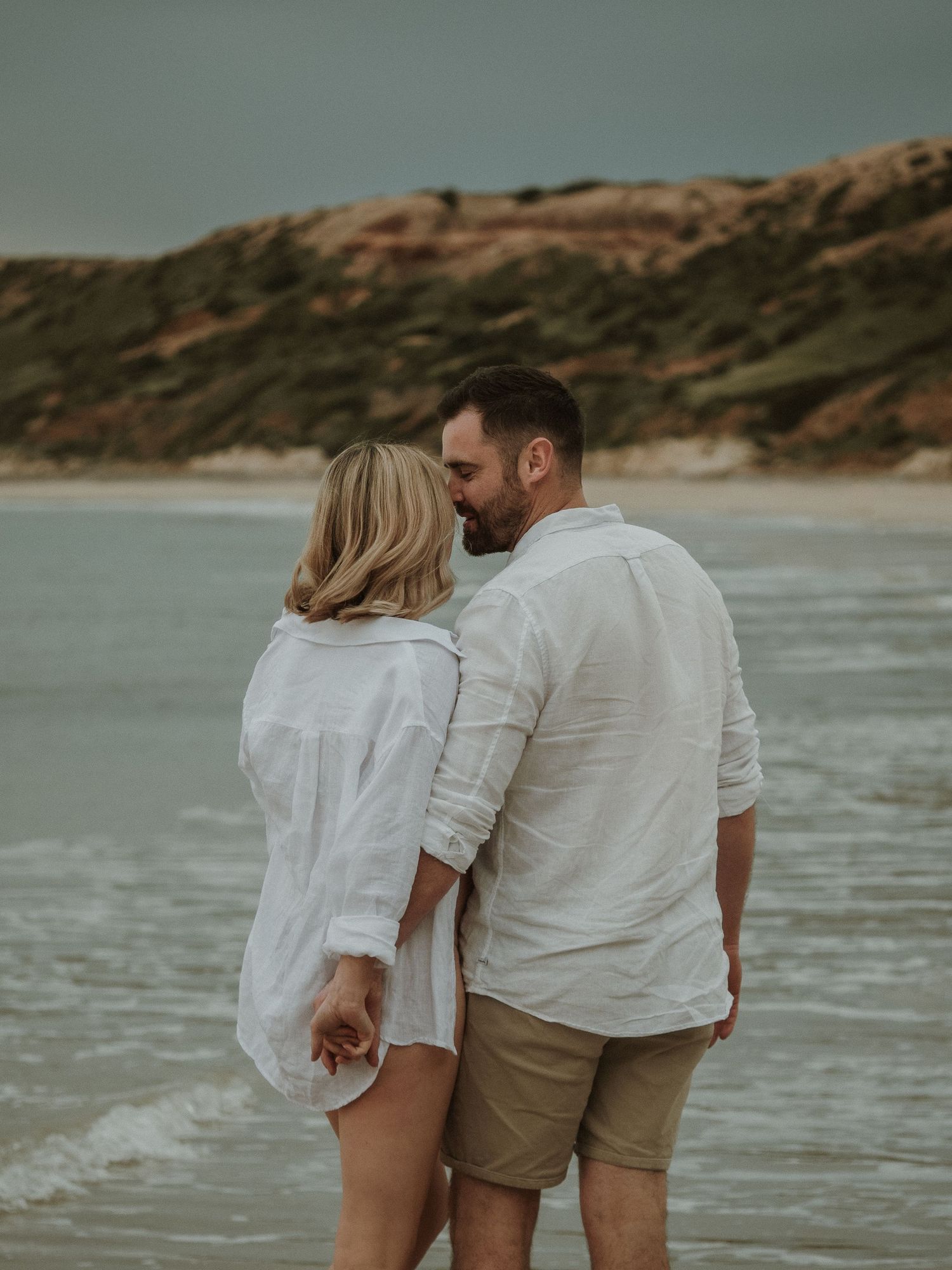 Couple walking together along beach with dramatic cliffs in background.