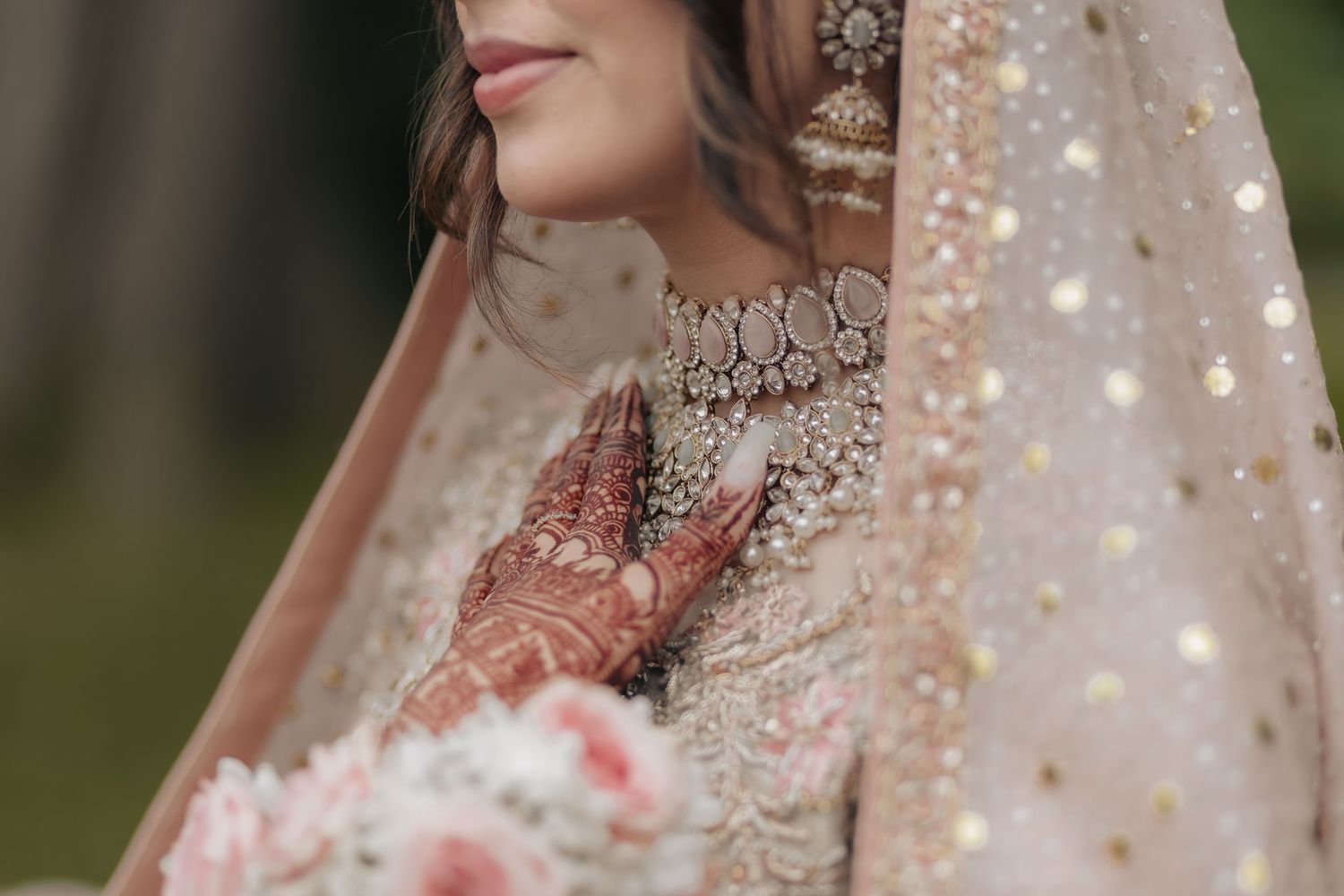 Close-up of bride wearing traditional South Asian jewelry and embroidered veil.