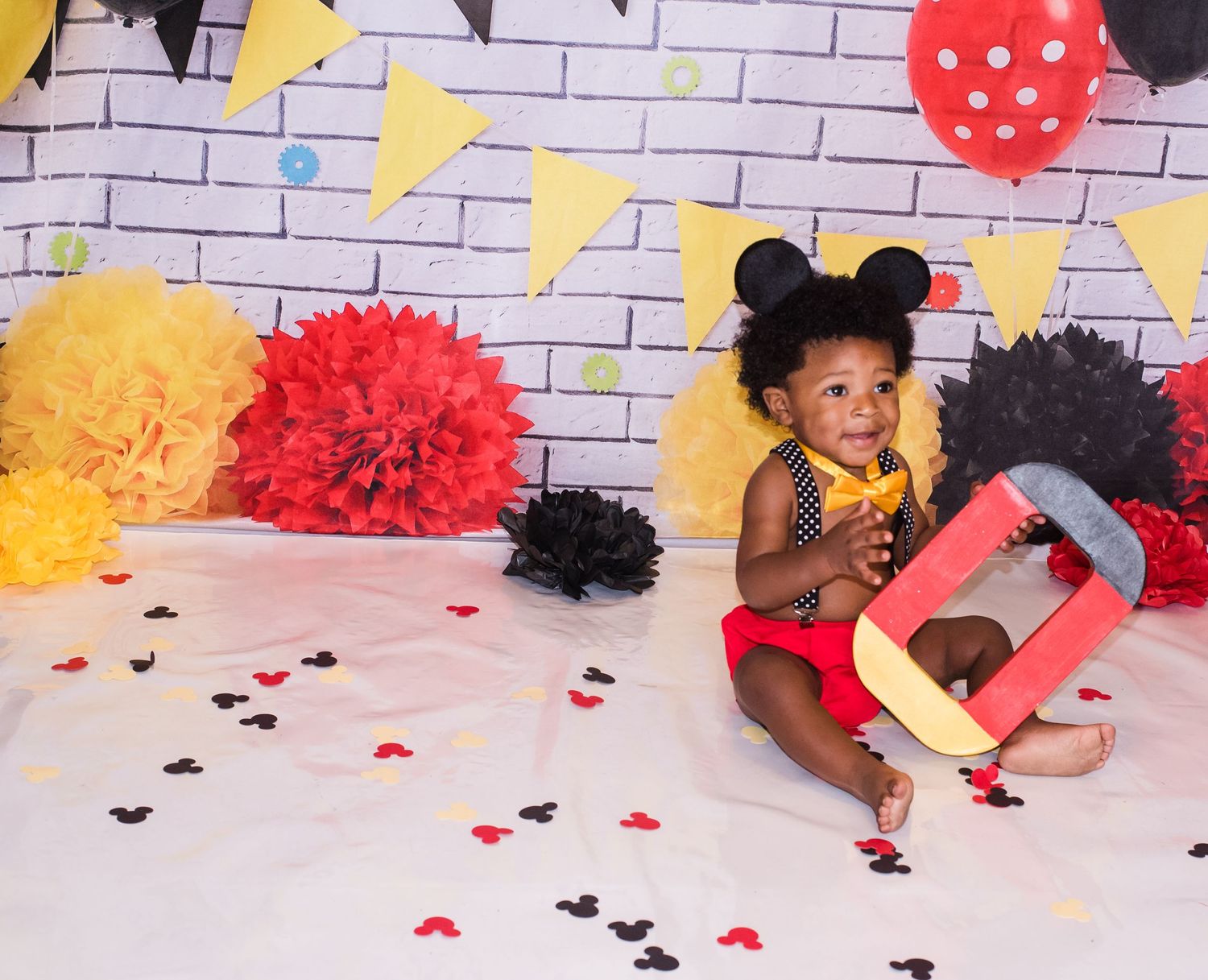Mickey Mouse themed party setup with colorful pom poms and brick wall backdrop.