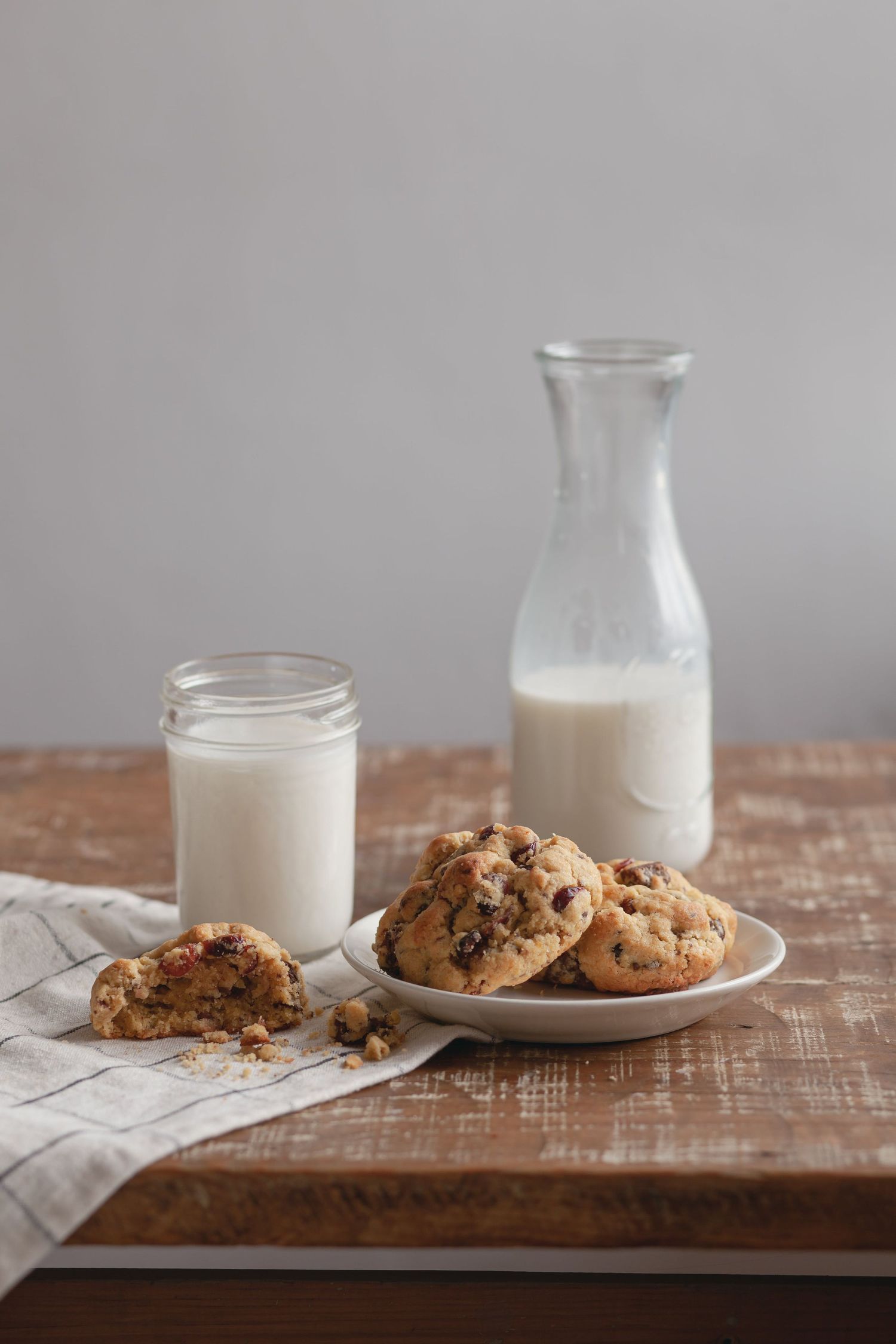 Fresh baked chocolate chip cookies served on plate with milk bottles on rustic wooden table.